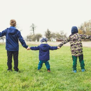 three children holding hands standing on grasses